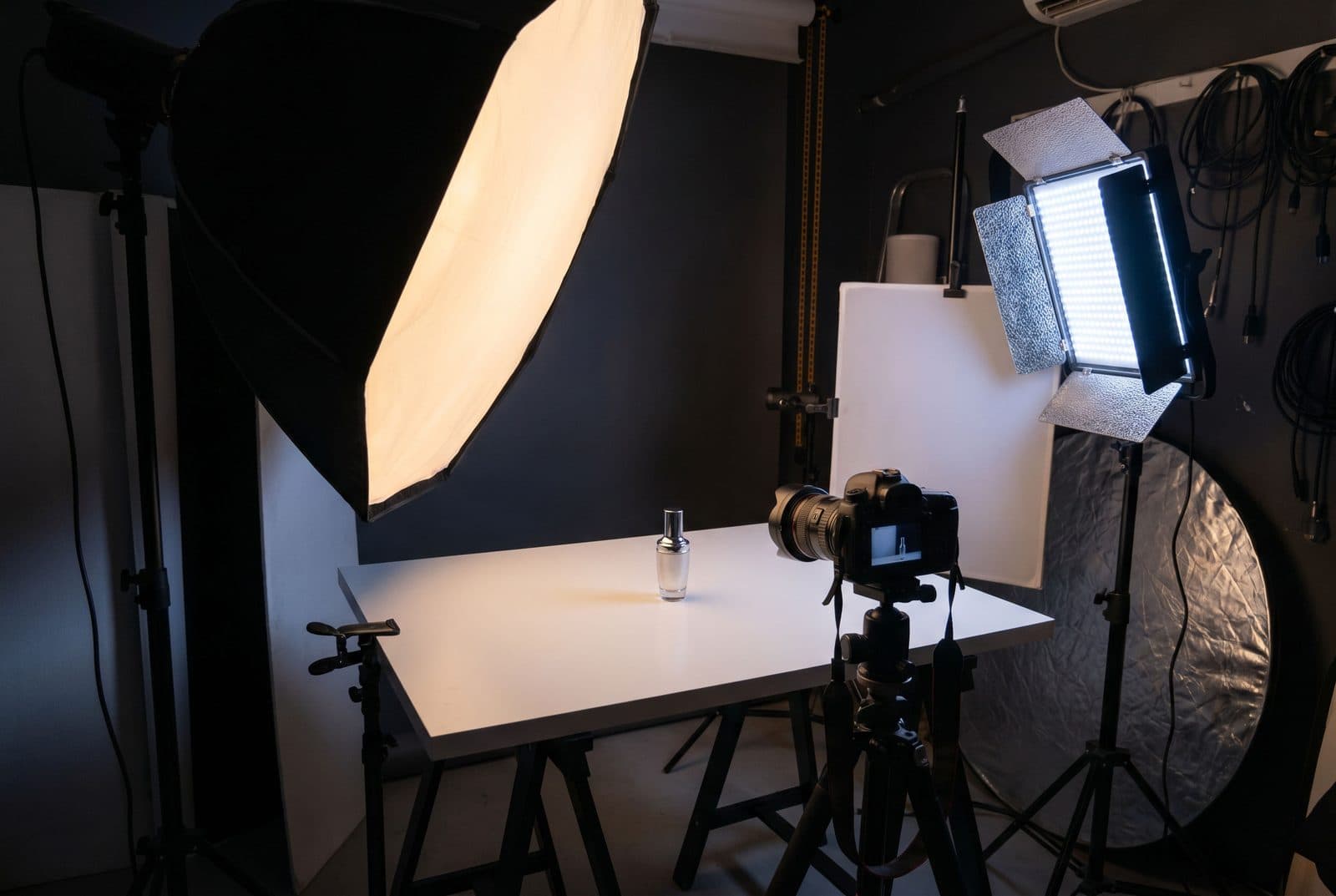 Set de toma de producto con softboxes, reflectores y cámara sobre trípode alrededor de un pequeño frasco
